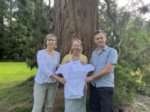 Women presented with cycling jersey in front of tree by male and female colleague